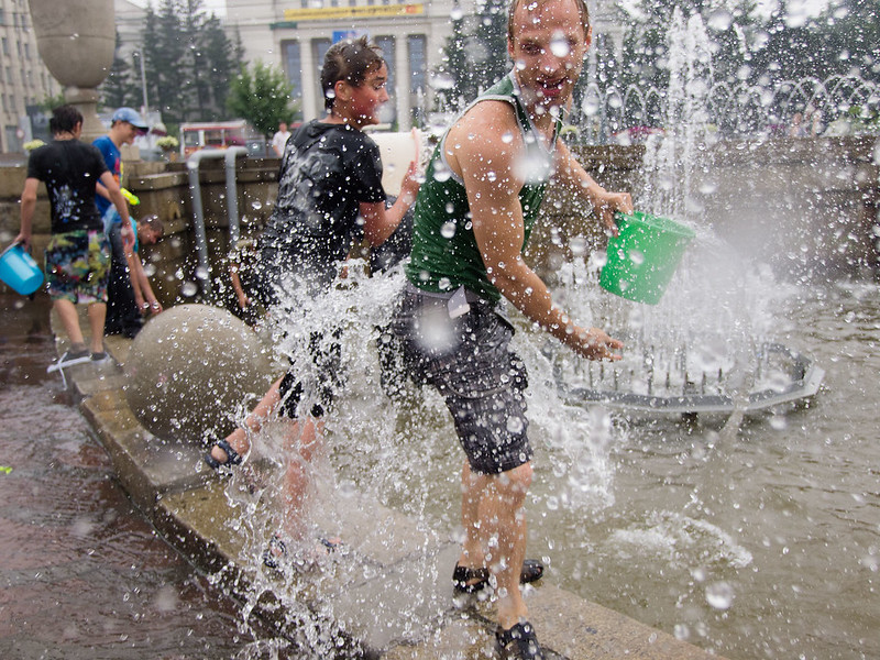 A group of people are laughing as they throw water from a fountain at each other. 