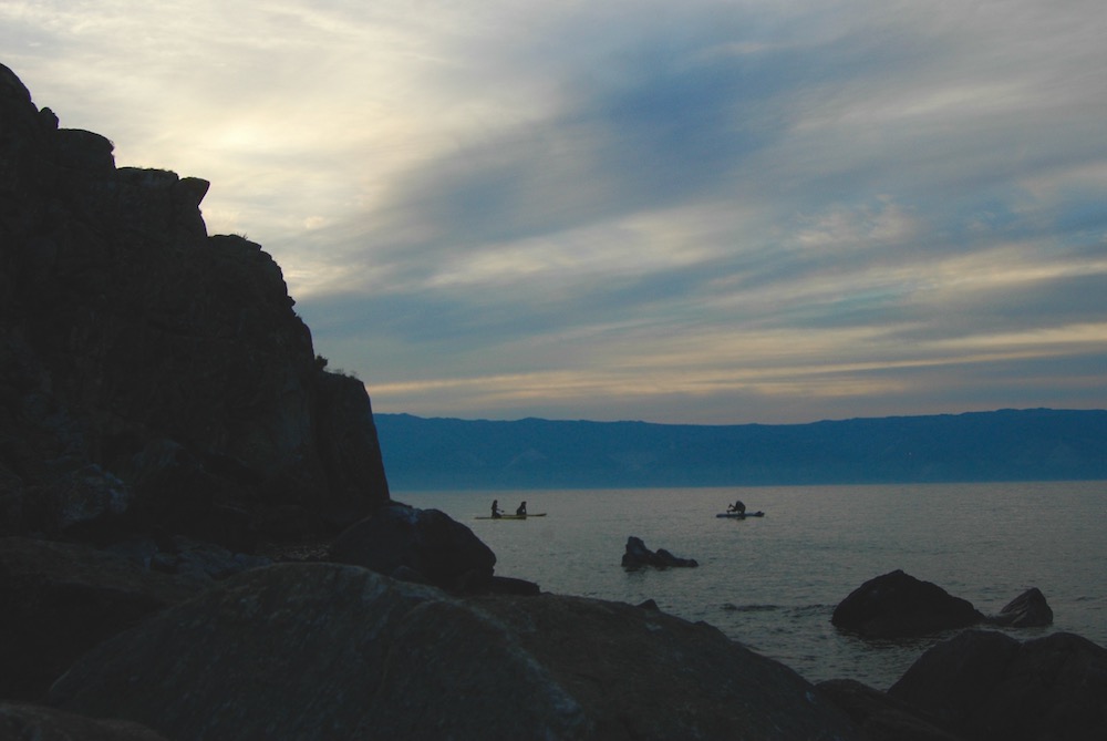 A couple paddleboarders float by shaman's rock in the sunset.