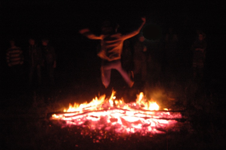 A blurry figure jumps over a fire in the dark of night.