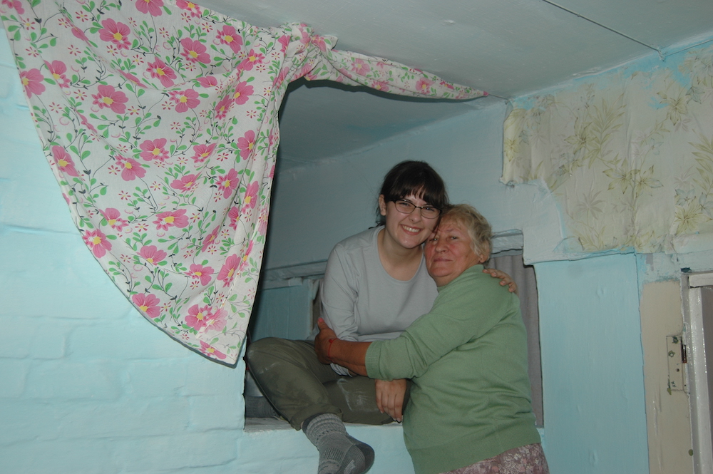 A girl sits on top of a white stove with a woman hugging her. 