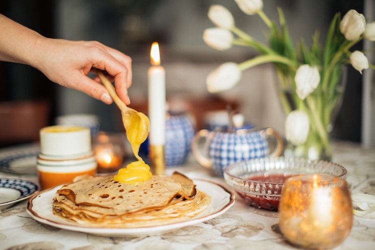 A beautiful stack of bliny sit on the table with a candle and tulip flowers.