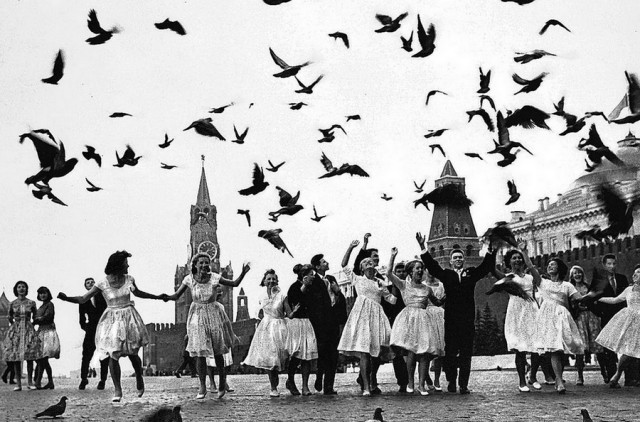a group of men and women in red square chasing a flock of doves
