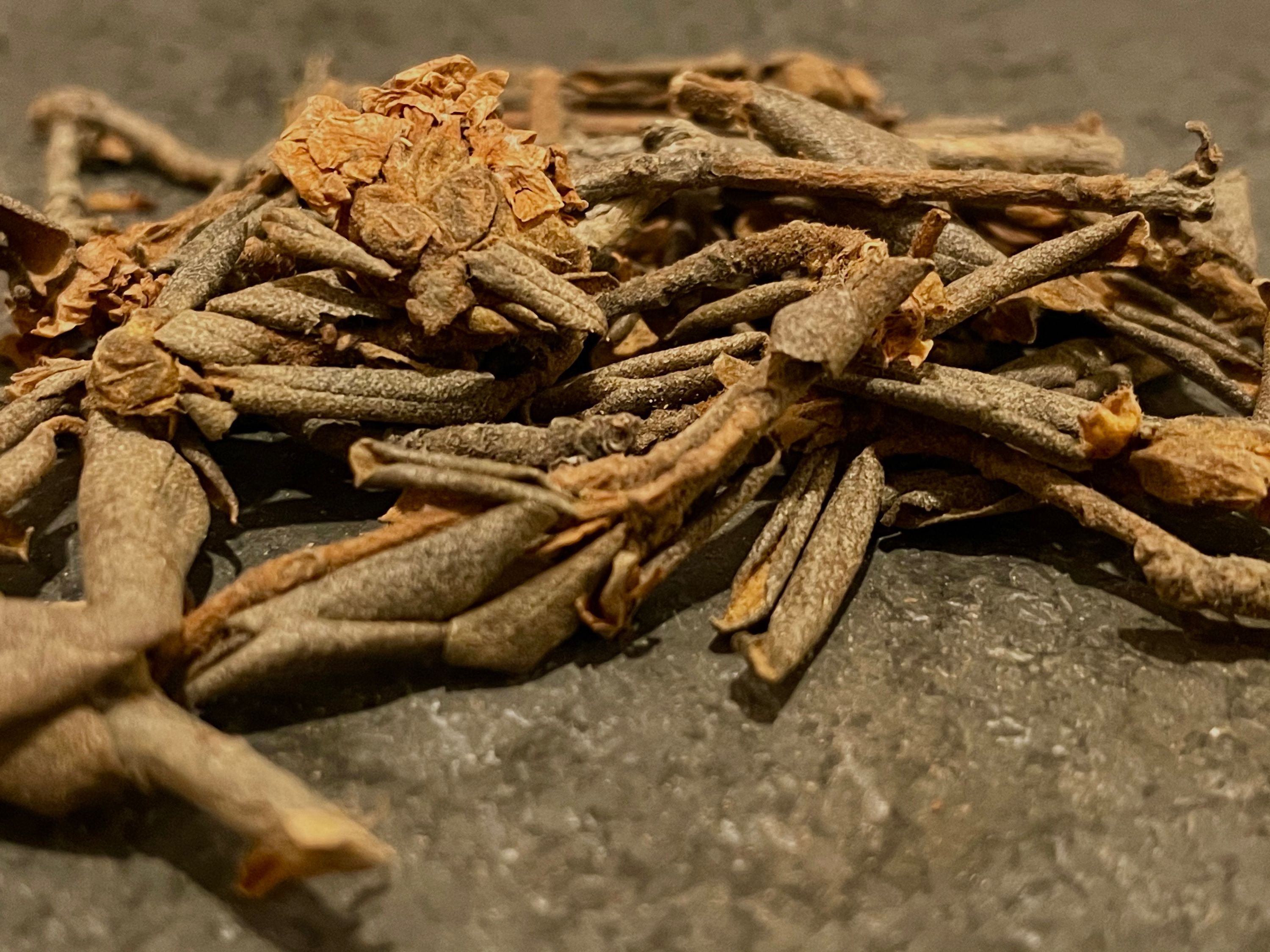 A brown pile of tea leaves and branches sits on a slate rock.