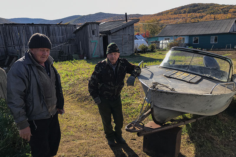 Two men standing near a boat on land.