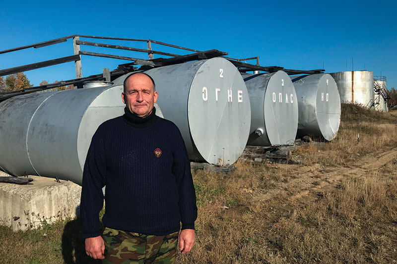 Georgy Konovalov, an attendant at a private gas station on the site of a former fuel storage facility, stands in front of empty storage tanks. 