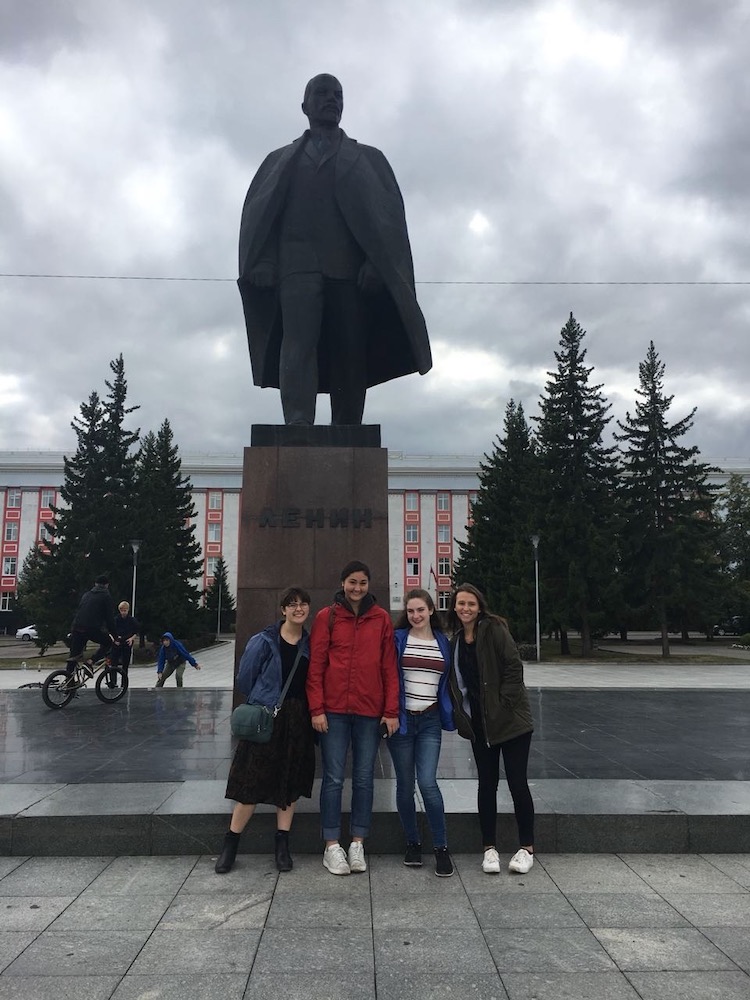 Students pose on a city street in front of a statue of Lenin. 