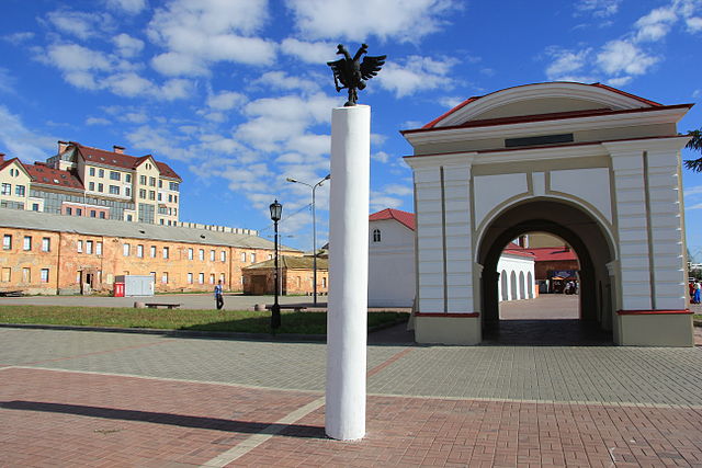 A green gate with a pole in front. On the pole there is an eagle statue. 