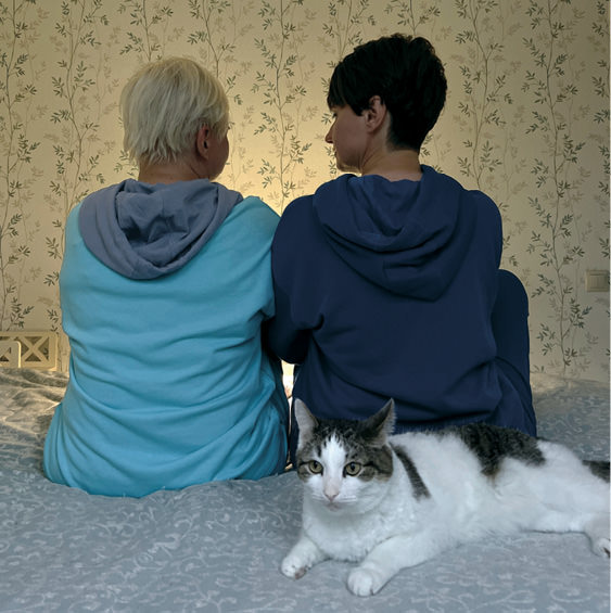 Two people sit on bed with backs to camera.