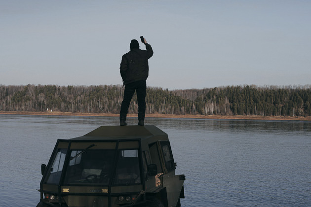 Man standing on car trying to get a cell signal.