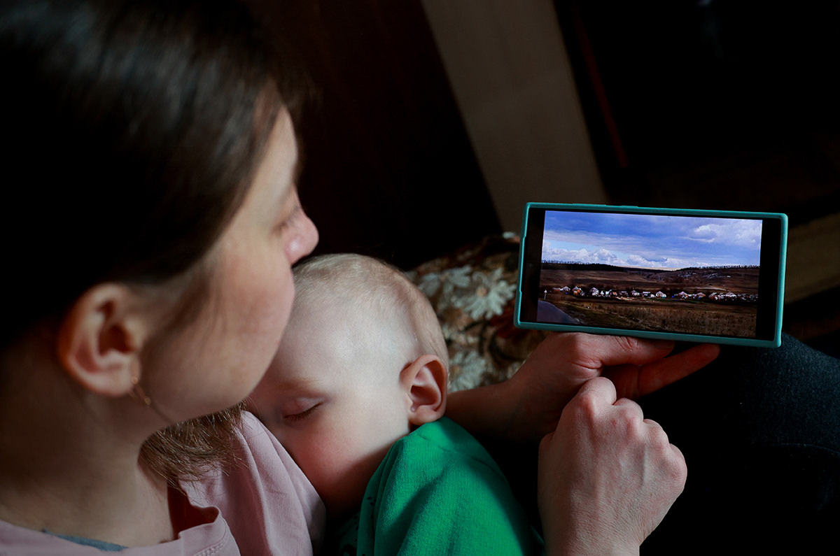 Woman looking at phone while holding infant.