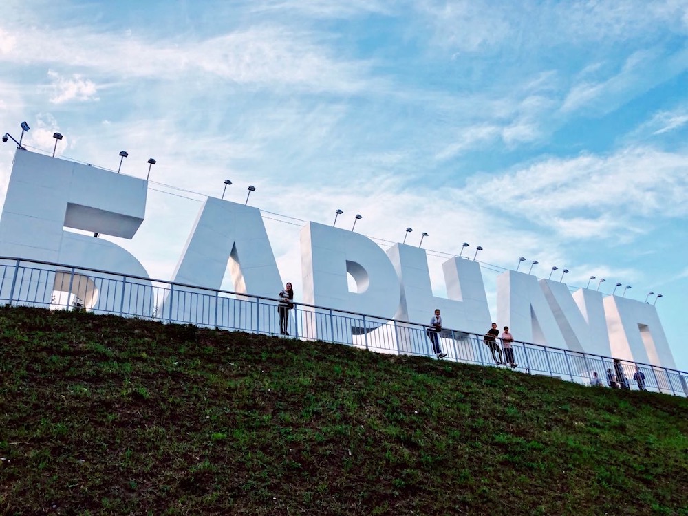 Students pose next to big white letters which spell out "BARNAUL" in cyrillic.